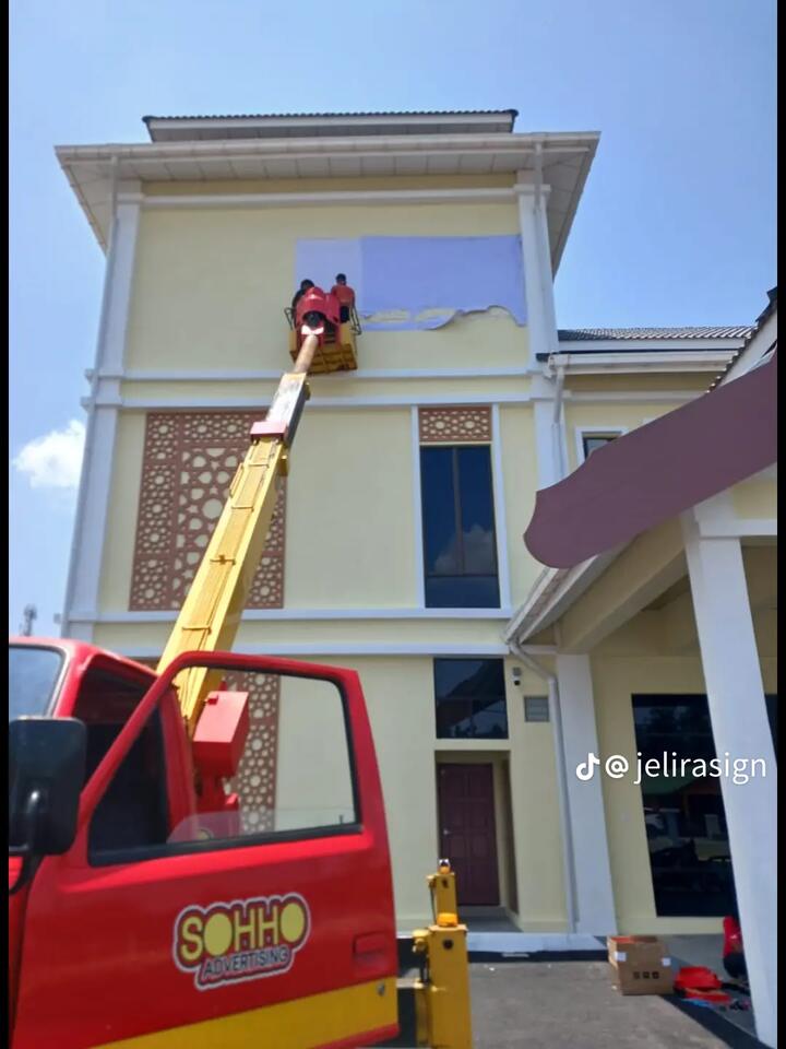 Pekerja di bakul skylift memasang papan tanda pada dinding bangunan